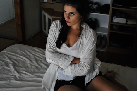 Woman sitting on a bed with crossed arms looking accusatory. 
